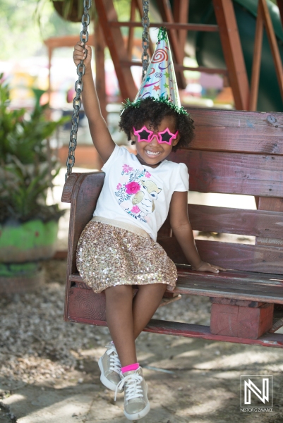 Celebrating a joyful birthday in Curacao with a young girl on a swing wearing a festive party hat