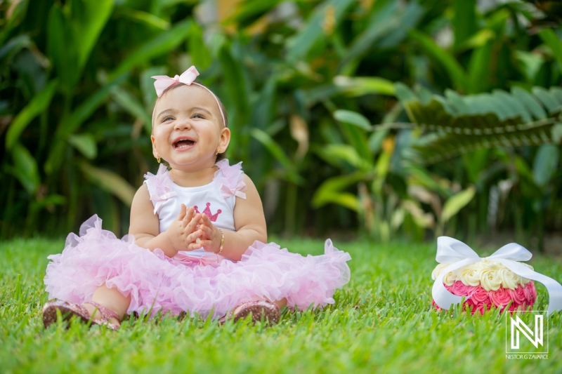 Birthday celebration for a smiling baby girl in Curacao surrounded by lush greenery and vibrant flowers during a sunny day