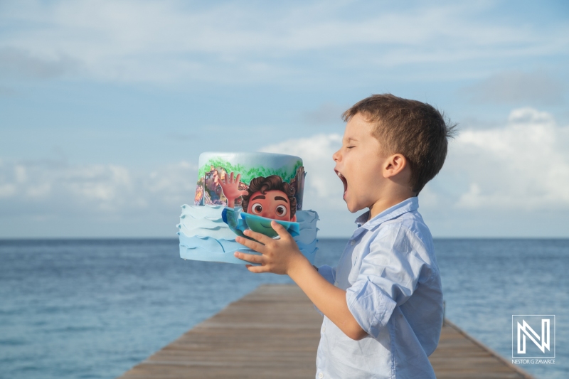 Birthday celebration in Curacao featuring a joyful boy with a themed cake on a beautiful pier