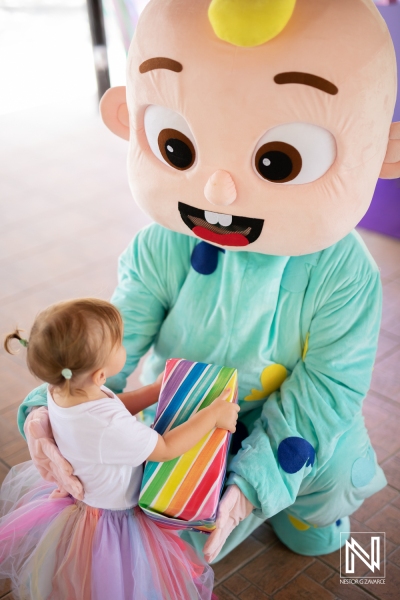 Celebration in Curacao with a colorful birthday theme featuring a joyful child receiving a gift from a cheerful character mascot