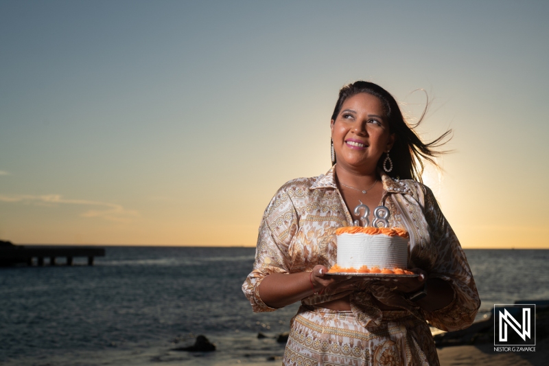 Birthday celebration on the beach in Curacao with a beautiful sunset and a joyful woman holding a cake