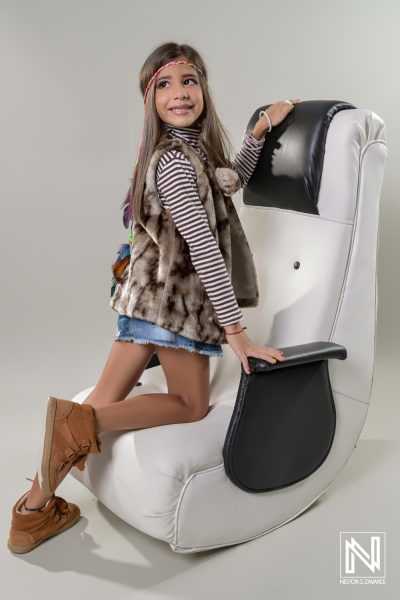 Young girl poses playfully on stylish chair during commercial shoot in Venezuela, showcasing vibrant fashion and lively spirit