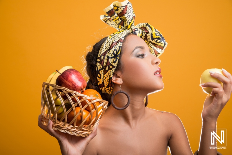 Woman showcasing a basket of colorful fruits against a vibrant orange background in Curacao