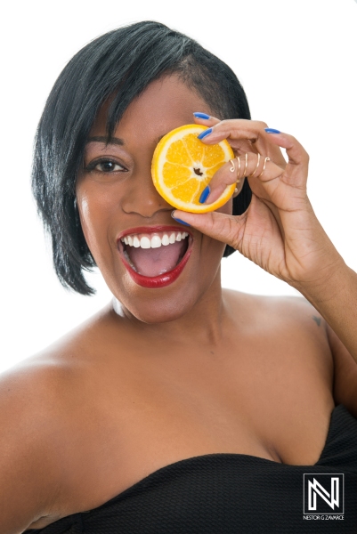 Smiling woman holding an orange slice in front of her eye in a vibrant commercial setting in Curacao