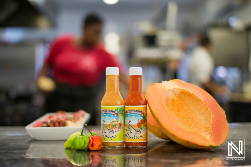 Bottles of hot sauce in a kitchen setting on Curacao with fresh papaya and peppers in focus