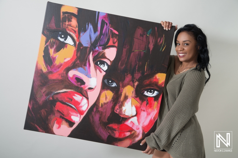 Colorful art piece showcasing diverse faces held by a smiling woman in Curacao promoting local creativity and cultural expression