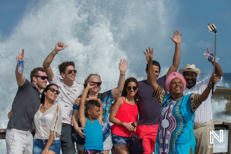 Group of friends celebrating by the ocean in Curacao with joyful expressions and a dramatic wave background