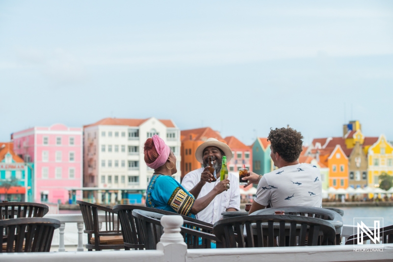 Friends enjoy refreshing drinks at a lively waterfront location in Curacao with colorful buildings in the background