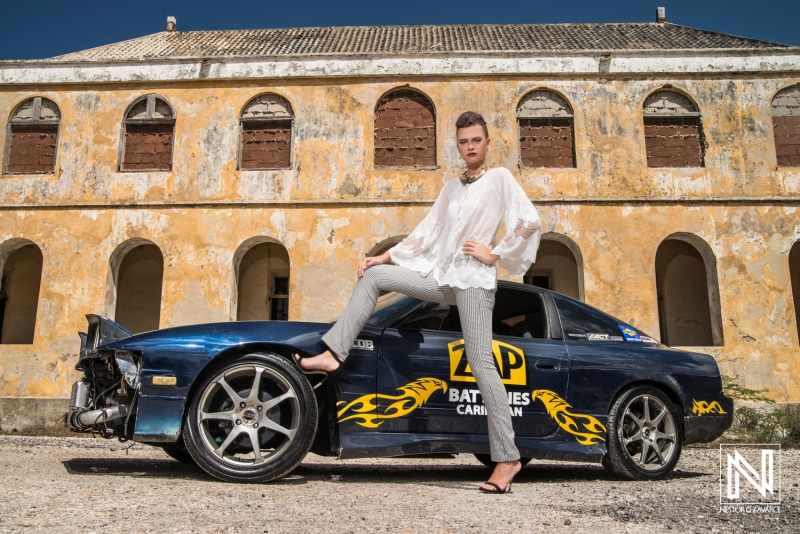 Model poses confidently by a modified car in a historic Curacao location showcasing a vibrant brand aesthetic and Caribbean flair