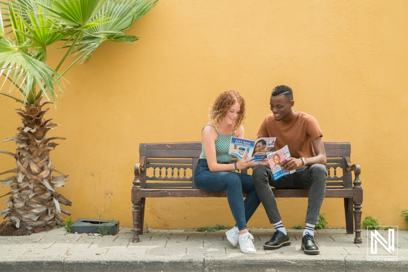 Couple engages with travel guide while relaxing on a bench in Curacao, showcasing the vibrant atmosphere of the island