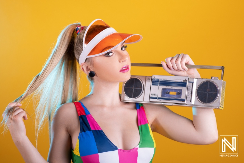 Vibrant young woman posing with a boombox against a bright yellow backdrop in Curacao during a commercial shoot