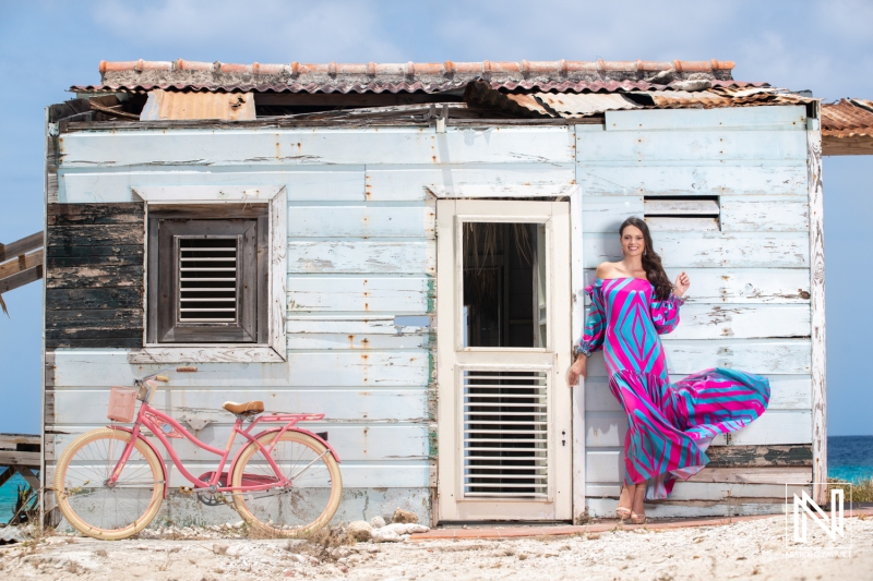 Vibrant summer fashion shoot in Curacao featuring a model near a colorful beachside shack with a vintage bicycle