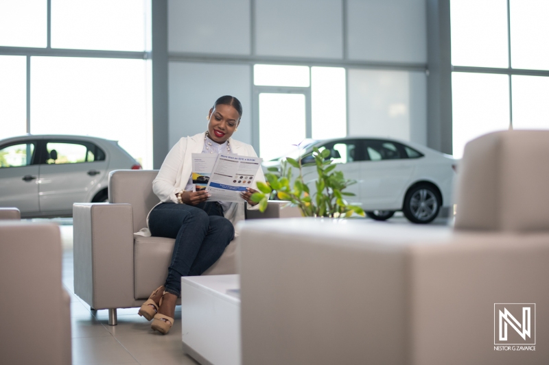 Woman reading a brochure in a car dealership in Curacao while seated comfortably near vehicles during daytime