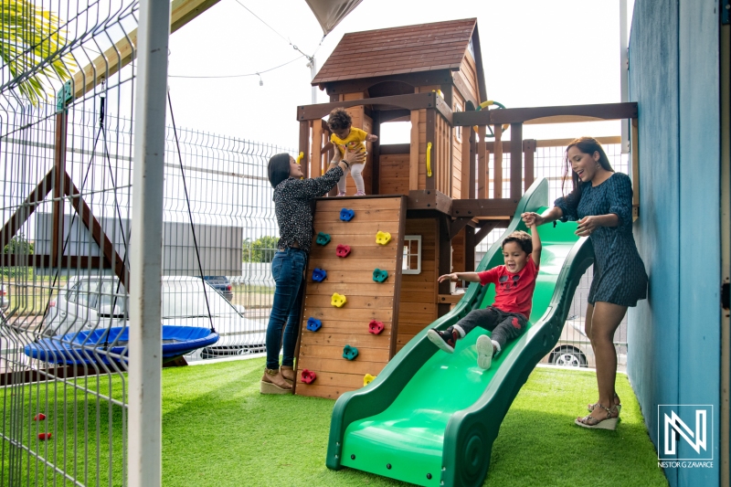 Family fun in Curacao with children enjoying a playground featuring a climbing wall and slide in a vibrant commercial area