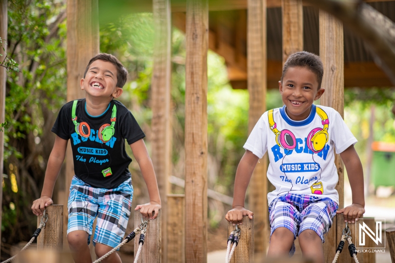 Two cheerful children playing on a wooden bridge in a vibrant outdoor setting in Curacao during a sunny day