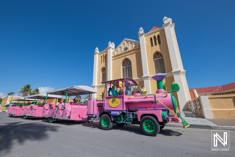 Colorful train tour passes by historic building in Curacao showcasing island culture and tourism