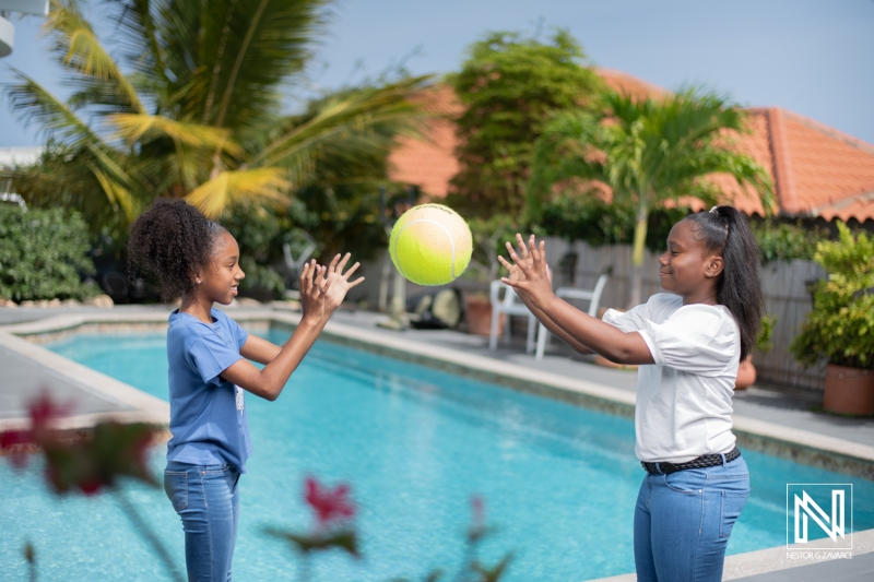 Children play catch with a yellow ball by the poolside in Curacao while enjoying the sunny weather