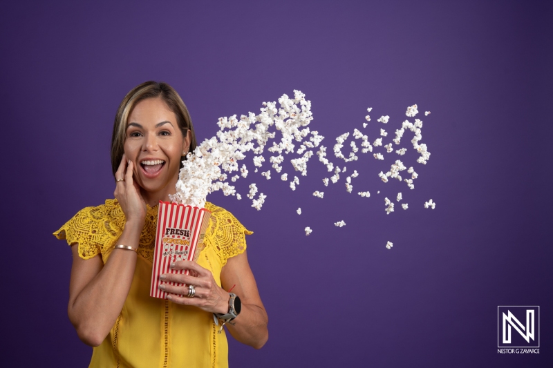 Excitement of popcorn flying out from a bucket held by a woman against a vibrant purple backdrop in Curacao