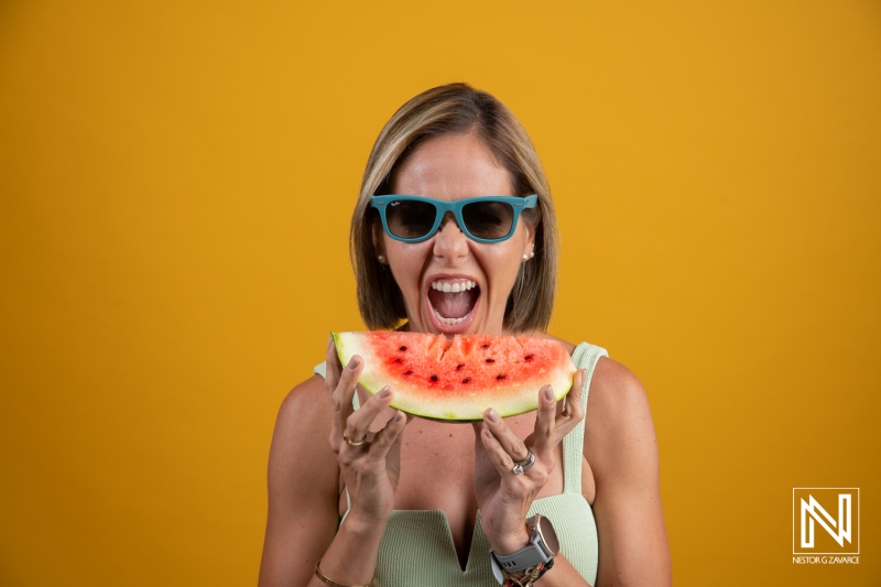 Enjoying fresh watermelon in Curacao against a vibrant yellow backdrop while wearing stylish sunglasses