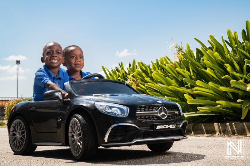 Young boys enjoying a fun ride in a toy car under the bright sun in Curacao while celebrating with friends