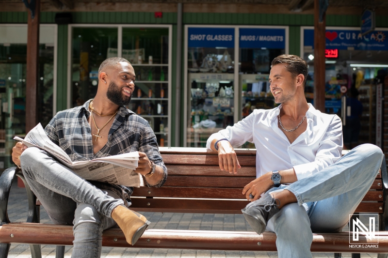 Two friends enjoying a sunny day in Curacao while reading and chatting, surrounded by local shops and vibrant atmosphere