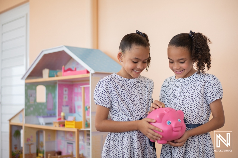 Two girls joyfully saving money in a pink piggy bank in a colorful playroom in Curacao, showcasing their creativity and teamwork in a playful environment