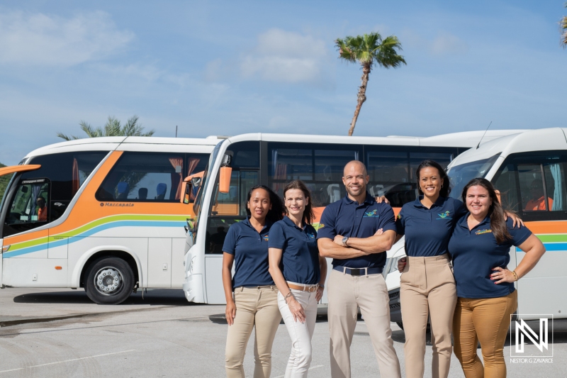 Team members pose confidently alongside branded buses in Curacao during a sunny day while promoting local transport services