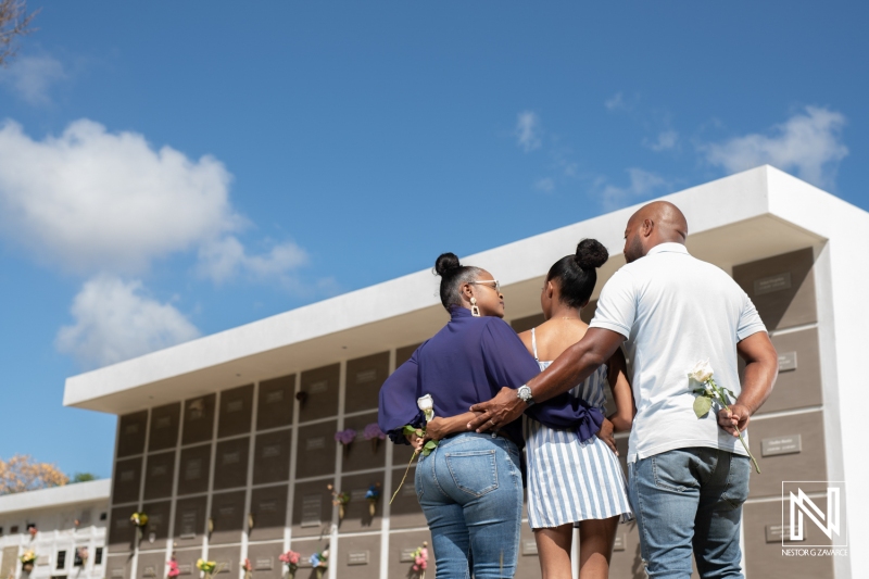 Family tribute at a cemetery in Curacao, honoring loved ones while holding flowers on a sunny day