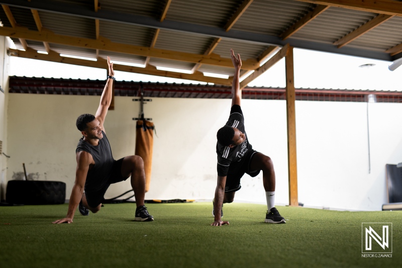 Physical fitness training session in Curacao showcasing strength and flexibility exercises with two individuals on turf