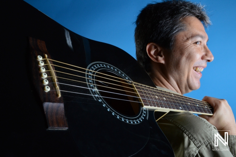 A Man Smiles While Holding a Black Acoustic Guitar Against a Blue Background, Showcasing His Passion for Music During a Leisure Activity