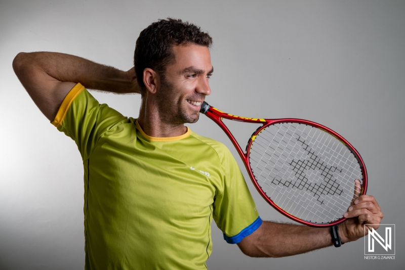 A Tennis Player Poses Joyfully With a Racket in a Studio, Showcasing Athleticism and a Vibrant Green and Yellow Sports Shirt During a Casual Photoshoot