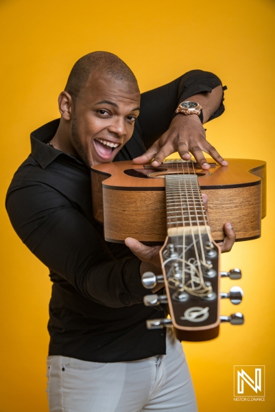 A Joyful Musician Poses With an Acoustic Guitar Against a Vibrant Yellow Background, Showcasing His Passion for Music in a Lively Studio Setting