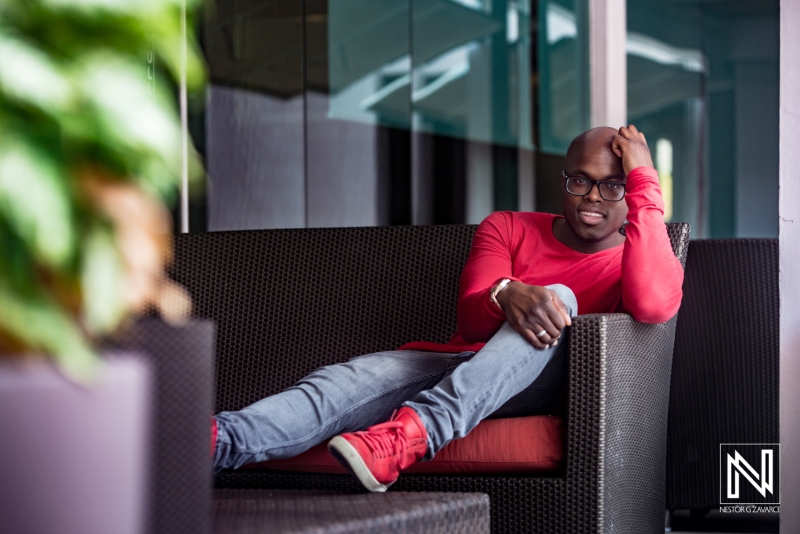 A Man Lounging Casually on a Modern Sofa in a Stylish Indoor Setting, Wearing a Red Shirt and Jeans While Enjoying a Moment of Relaxation