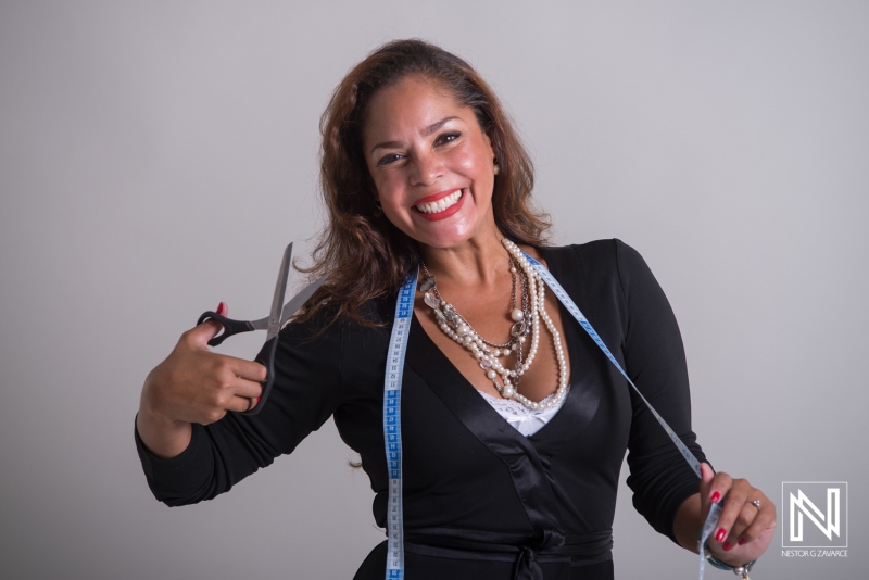 A Woman Smiles Brightly While Holding Scissors in One Hand and a Measuring Tape in the Other, Showcasing Her Enthusiasm for Fashion Design in a Bright, Neutral Studio Setting