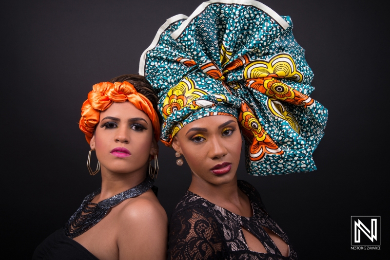 Two Women Pose Side by Side, Showcasing Vibrant Head Wraps and Unique Fashion Styles Against a Dark Backdrop in an Artistic Portrait Captured Indoors