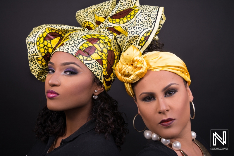 Two Women Showcase Vibrant Headwraps in a Studio Setting, Highlighting Traditional and Contemporary Styles With Striking Expressions and Coordinated Outfits