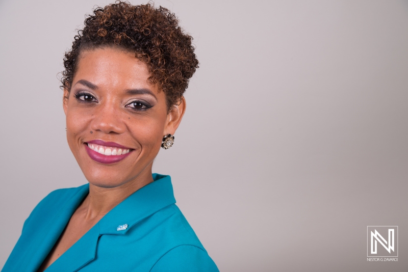 A Professional Woman With Curly Hair Smiles Confidently While Wearing a Blue Blazer, Posing Against a Neutral Background in a Friendly and Professional Environment