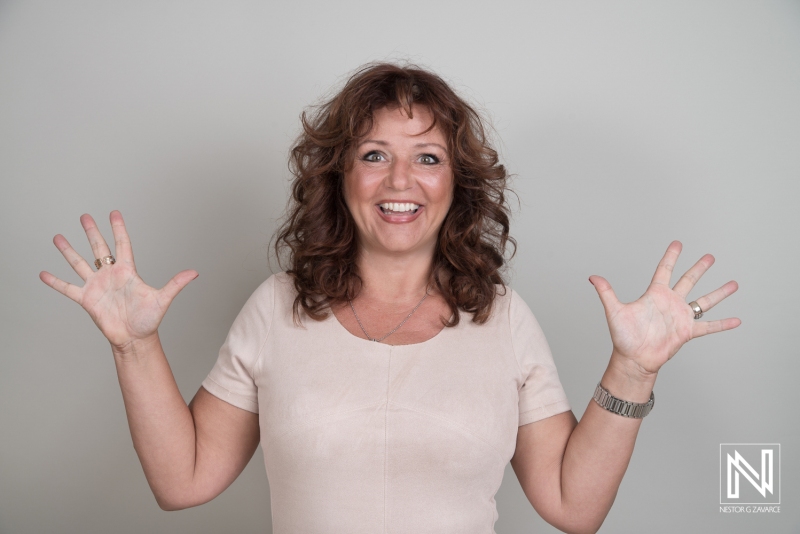 Cheerful Woman With Curly Hair Enthusiastically Raising Her Hands Against a Neutral Wall, Showcasing Excitement and Joy in a Casual Setting