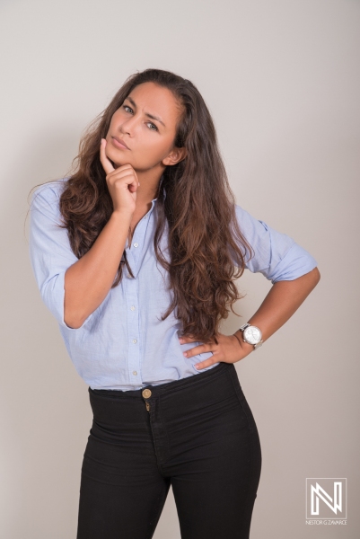 A Young Woman With Long Hair Poses Thoughtfully in a Light Blue Shirt and Black Pants, Showcasing a Confident Expression in a Minimalist Studio Setting