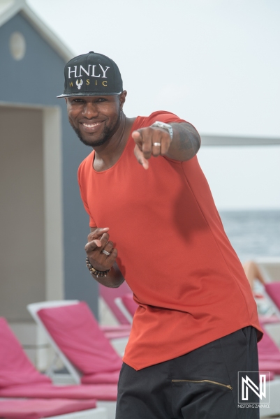 A Man in a Bright Red Shirt and Cap Joyfully Poses and Points at the Camera by the Poolside on a Sunny Day in a Tropical Resort Setting