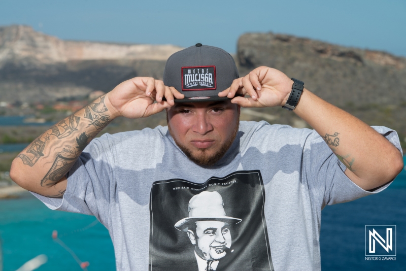 A Man Wearing a Hat Poses Confidently Outdoors Near a Coastal Landscape With Cliffs and Blue Water, Showcasing a Relaxed Attitude in Bright Sunlight