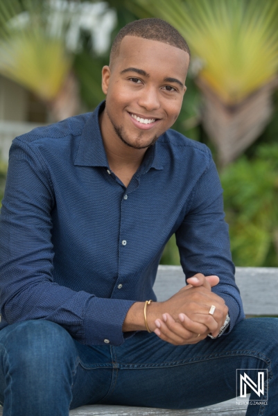 A Young Man Smiles Confidently While Seated Outdoors Among Tropical Foliage on a Sunny Day