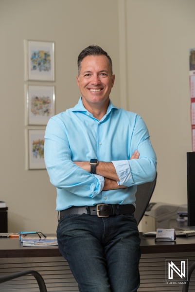 A Smiling Professional Man in a Light Blue Shirt Poses Confidently in His Office During the Day, Reflecting a Welcoming and Productive Work Environment