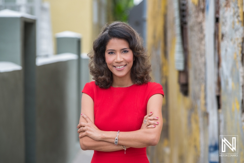 Confident Woman in a Red Dress Poses With Arms Crossed in a Narrow Alley, Showcasing a Vibrant Background and Warm Daylight