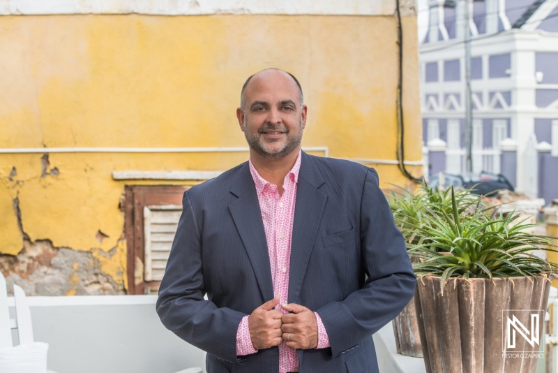 A Well-Dressed Man Poses Confidently Against a Rustic Backdrop in a Vibrant Outdoor Setting Under Bright Daylight