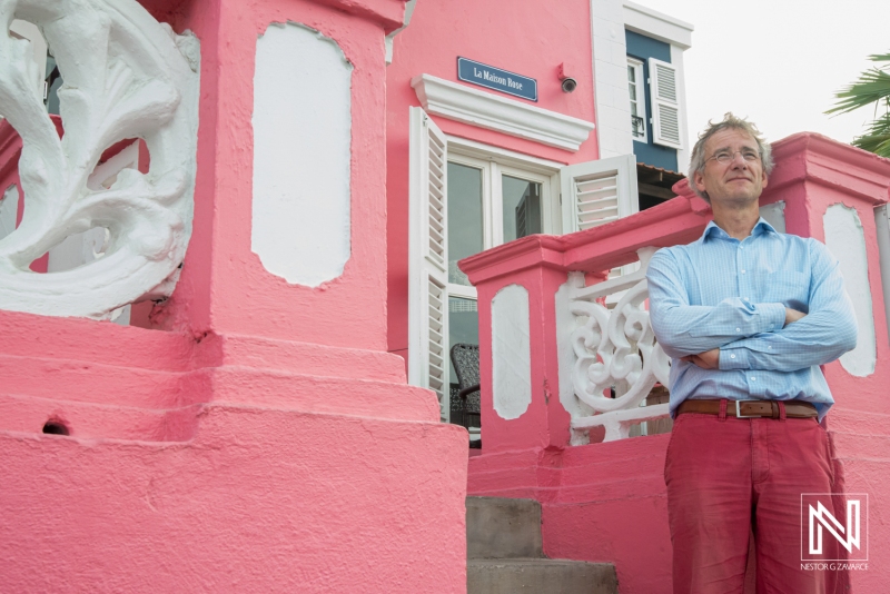 A Man Stands Confidently on the Steps of a Vibrant Pink Building in a Coastal Area, Enjoying the Warm Atmosphere and Beautiful Architecture During the Daytime