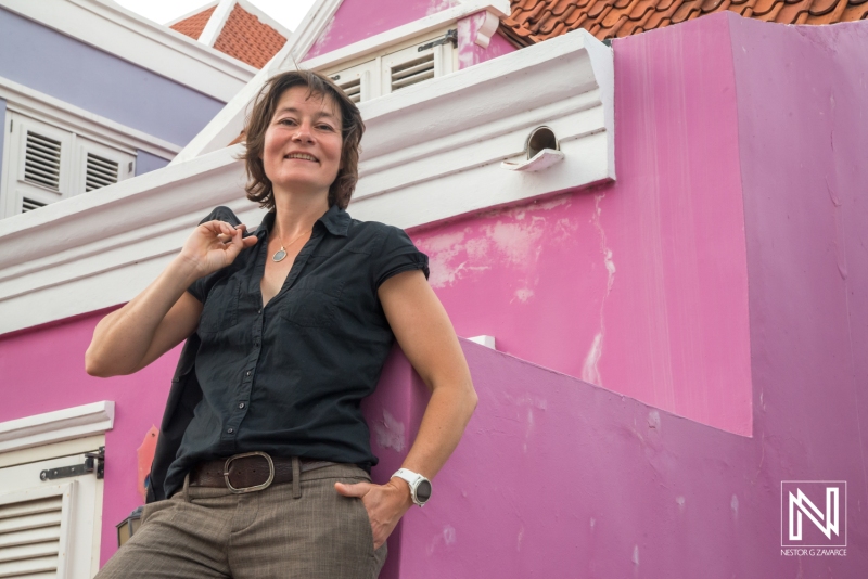 A Woman Poses Confidently Against a Colorful Wall in a Vibrant Outdoor Setting During Daylight, Showcasing a Joyful Moment of Exploration in a Lively Neighborhood