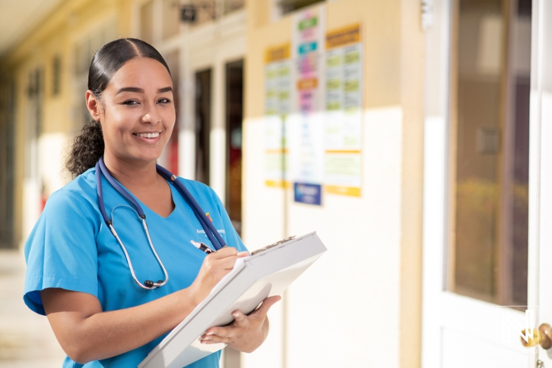 Young Healthcare Professional in Blue Scrubs Smiles While Taking Notes in a Medical Facility During the Day