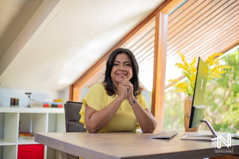 A Smiling Woman Dressed in Yellow Sits at a Desk in a Bright, Modern Workspace, Showcasing Her Creativity and Positive Energy During a Productive Workday