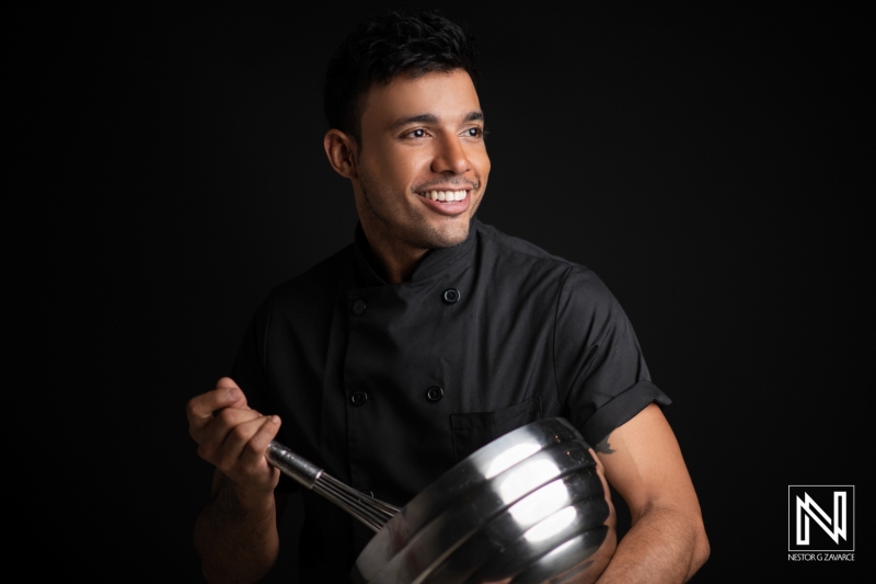 A Smiling Chef in a Black Uniform Holding a Whisk, Showcasing Culinary Passion and Expertise in a Professional Kitchen During an Evening Event